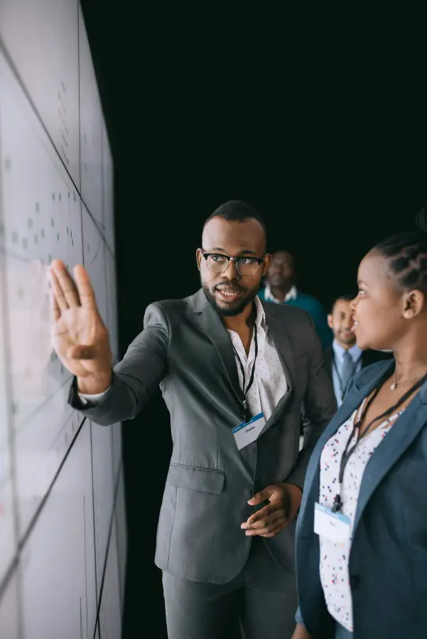 A tech-business consultant named Charles explains a data chart on a large display to a colleague at a professional confere...