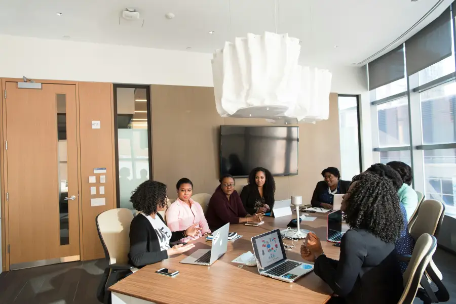 Group of professional women collaborating around a conference table with laptops during a tech-business strategy meeting.